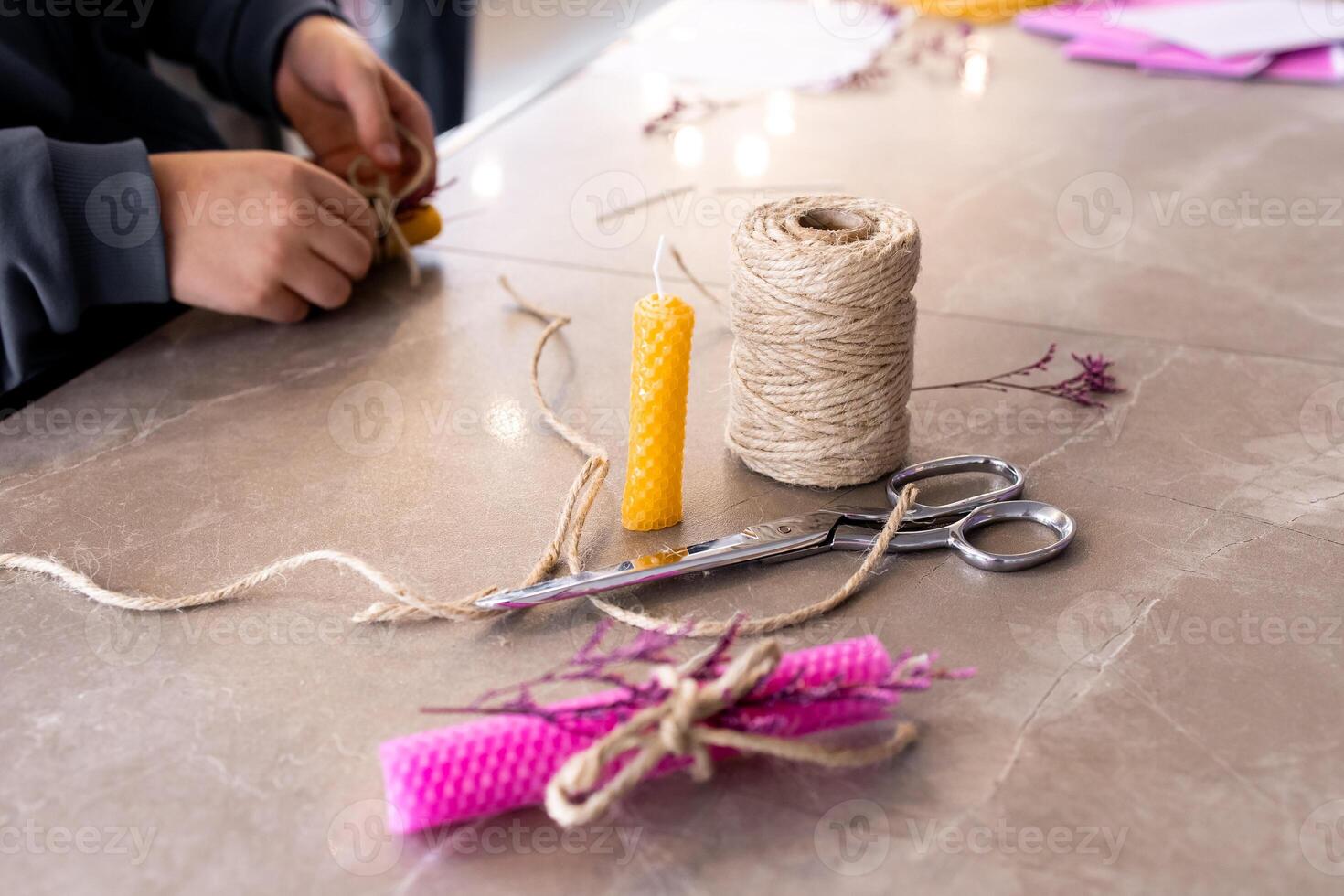 Young hands crafting beeswax candle with natural twine on marble surface photo