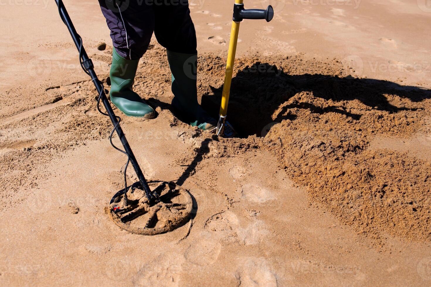 Metal detector enthusiast digging treasure on sandy beach photo