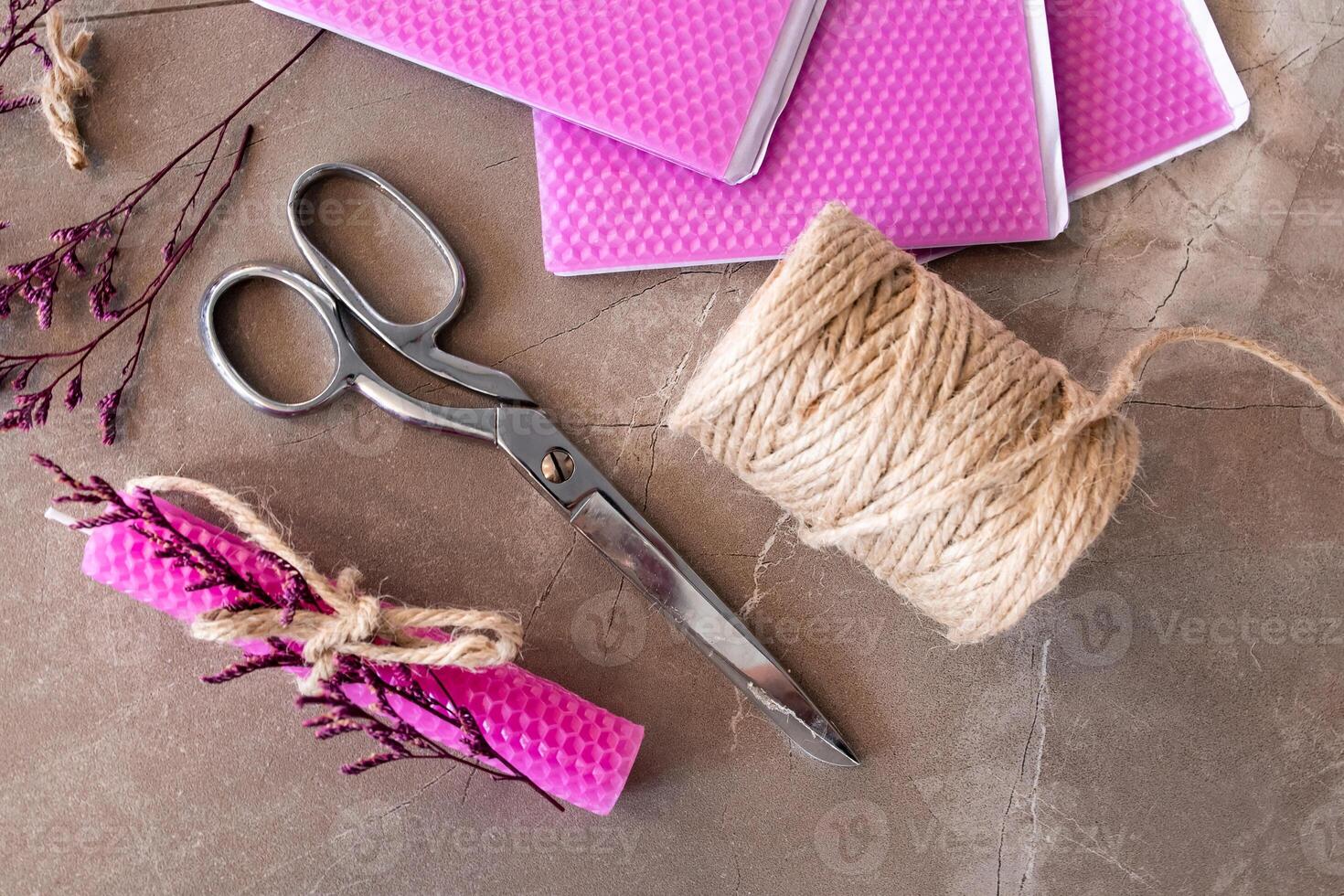 Crafting materials with pink wax sheets, scissors, jute twine, and dried flowers on stone surface photo