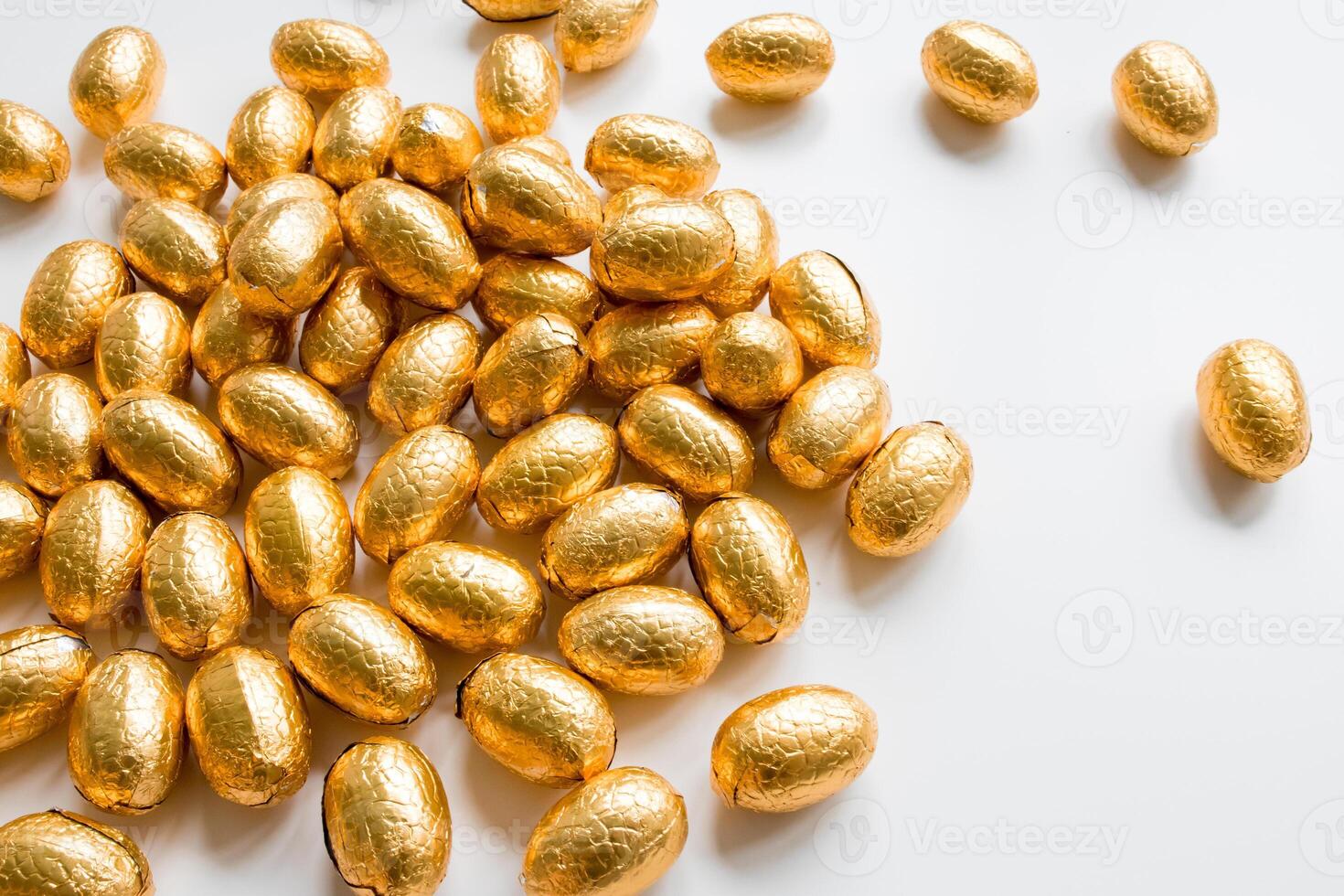 Pile of shiny golden foil wrapped chocolate eggs on white background photo