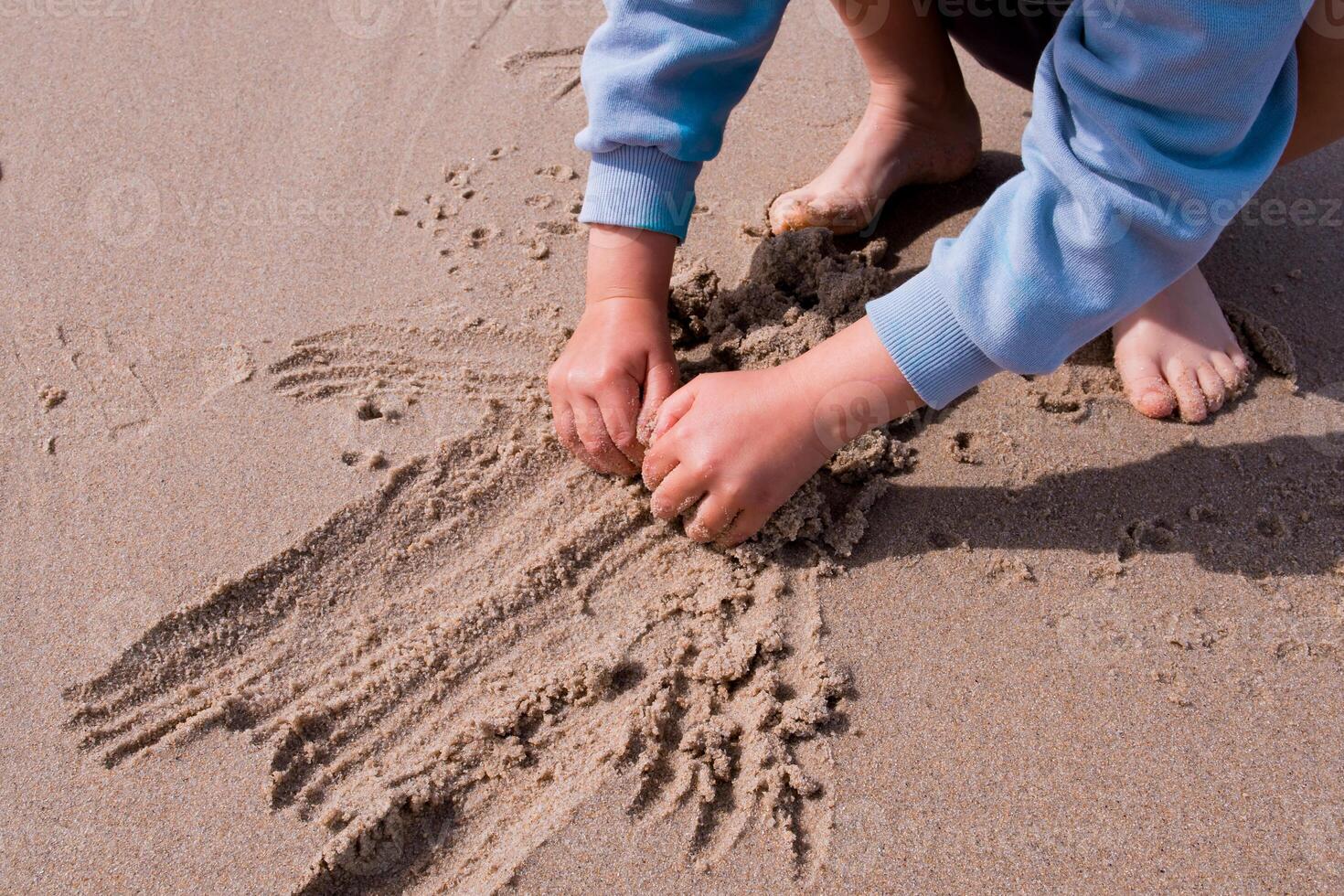 Child playing in sand at beach with hands and feet visible photo