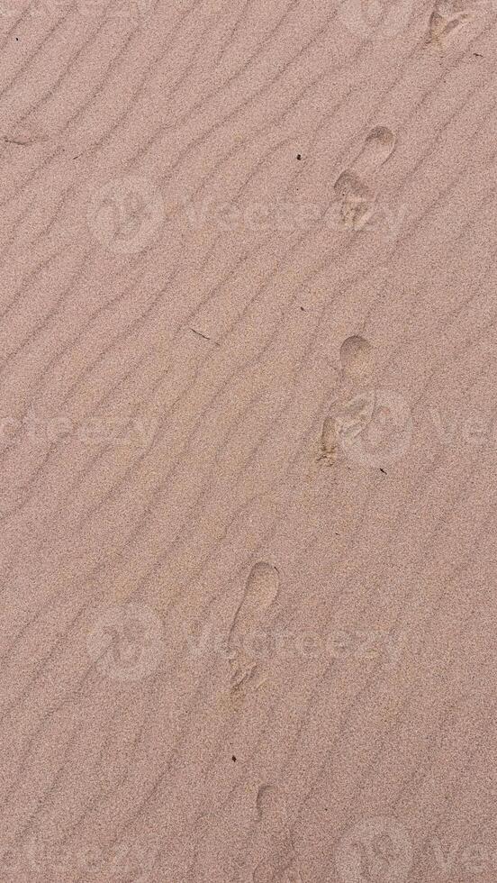 Sandy beach with footprints and gentle waves in sand texture photo