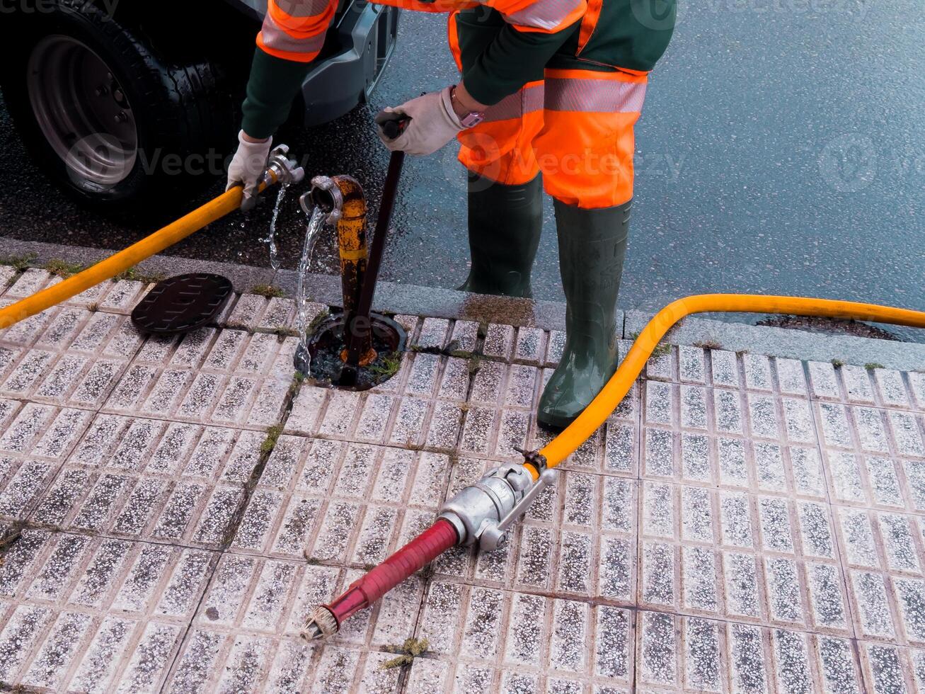 Worker in protective gear using hose for street drainage maintenance photo