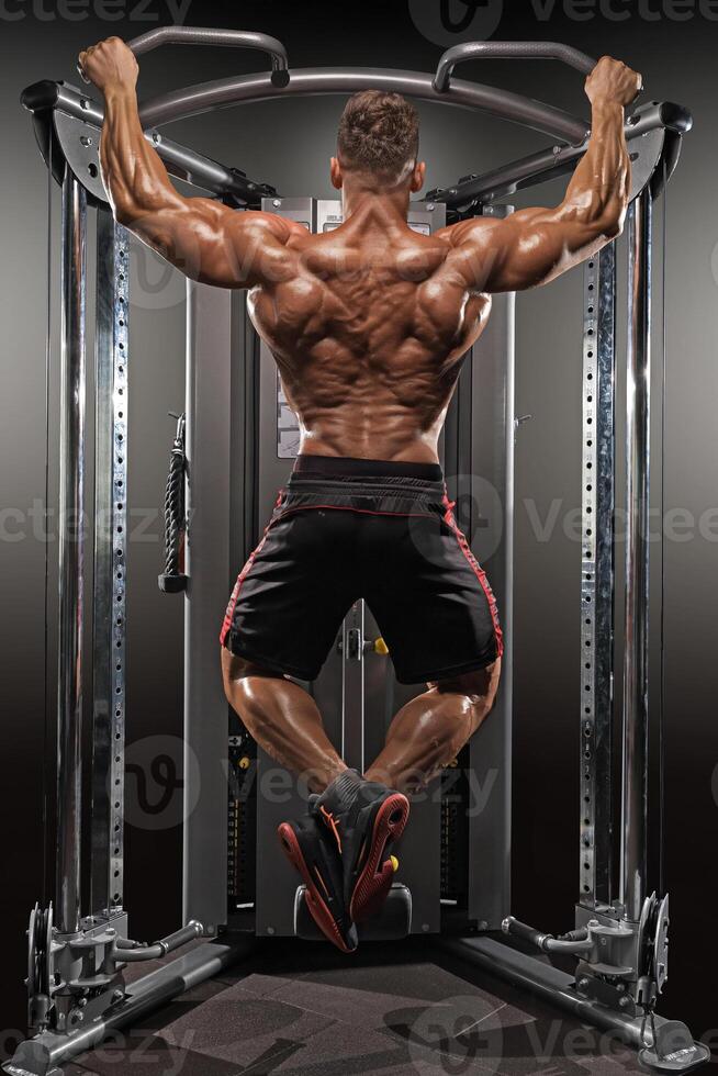 well built man performs pull ups on gym equipment strengthen his back and arms. environment is focused on fitness showcasing dedication health and strength training photo