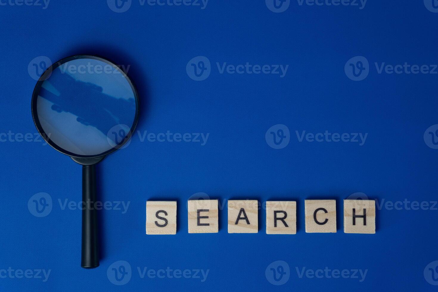 Magnifying Glass Next to Wooden Tiles Spelling Search on Blue Background photo