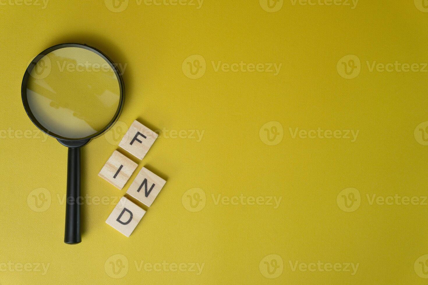 Magnifying Glass and Wooden Tiles Spelling Find on Yellow Background photo