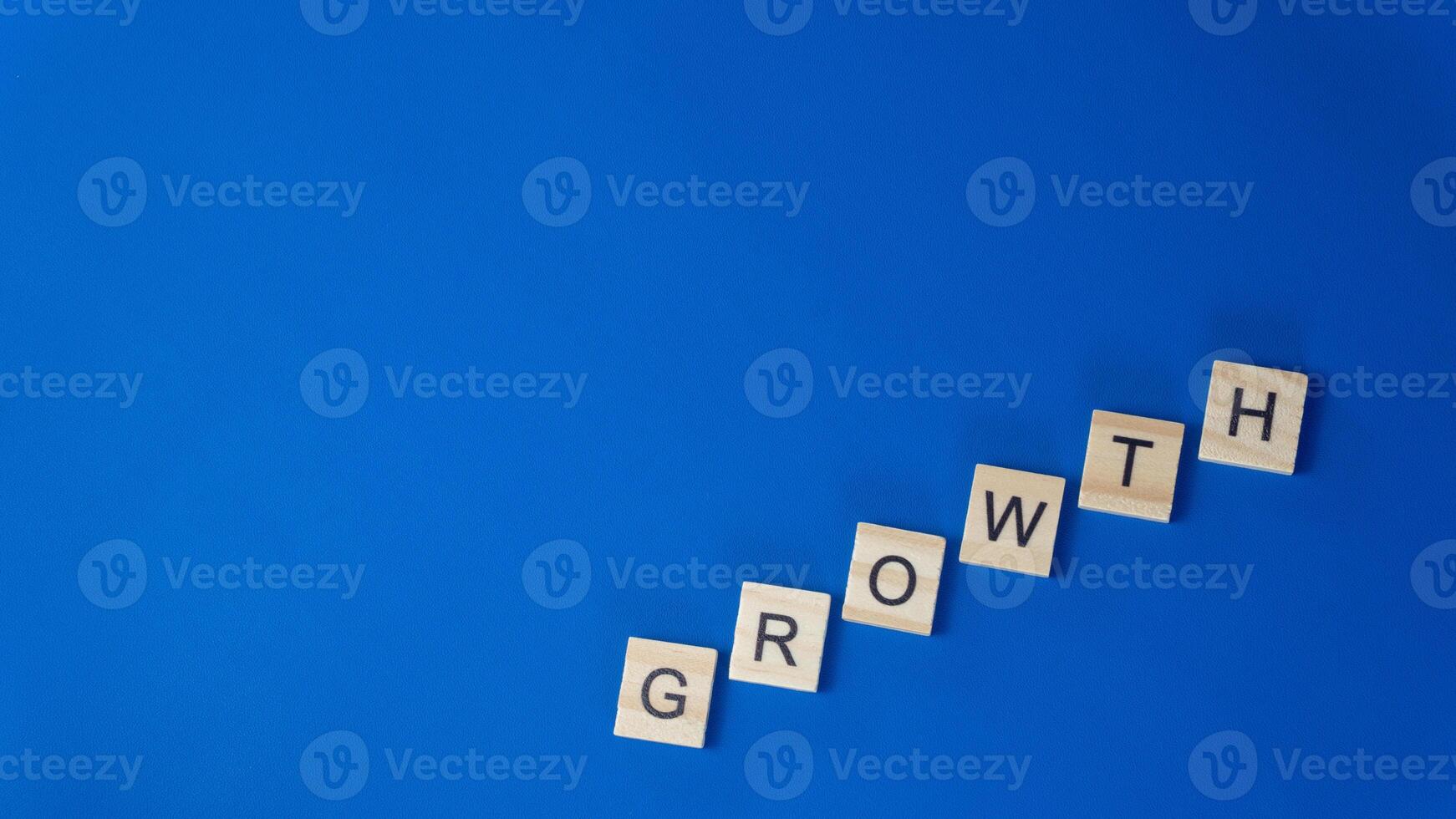 Word GROWTH Arranged Diagonally with Wooden Tiles on Blue Surface Progress and Development Theme photo