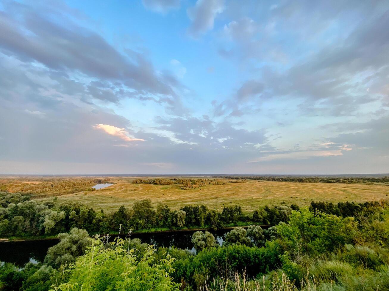 A scenic rural landscape with a river winding through a green valley, surrounded by trees and fields. The dramatic sunset sky and soft light create a peaceful and atmospheric countryside scene photo