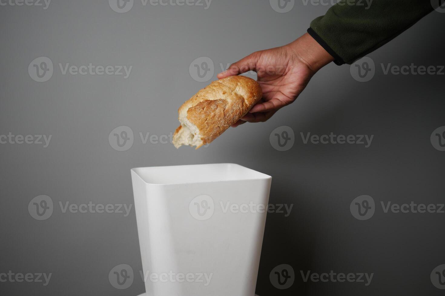 Hand discarding bread into a trash bin in a minimalistic setting photo