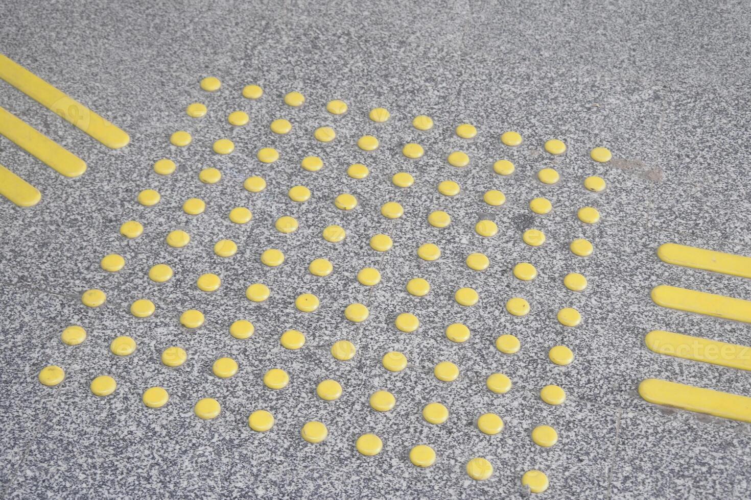 Textured ground surface with yellow tactile paving indicators photo