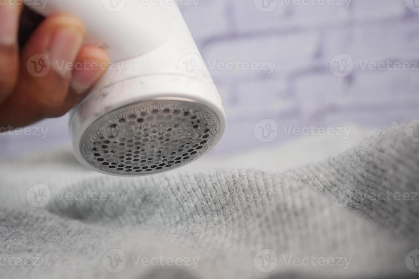 Handheld fabric shaver being used on a gray sweater to remove lint photo