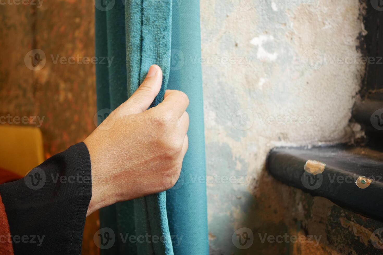 Hand adjusting a teal curtain near a window in a cozy interior photo