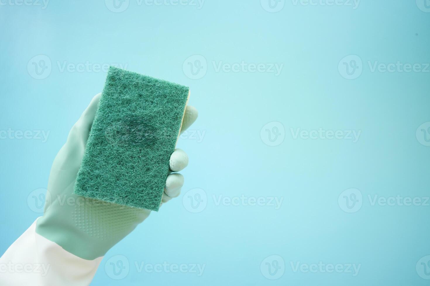 Cleaning sponge held by gloved hand against a blue background photo