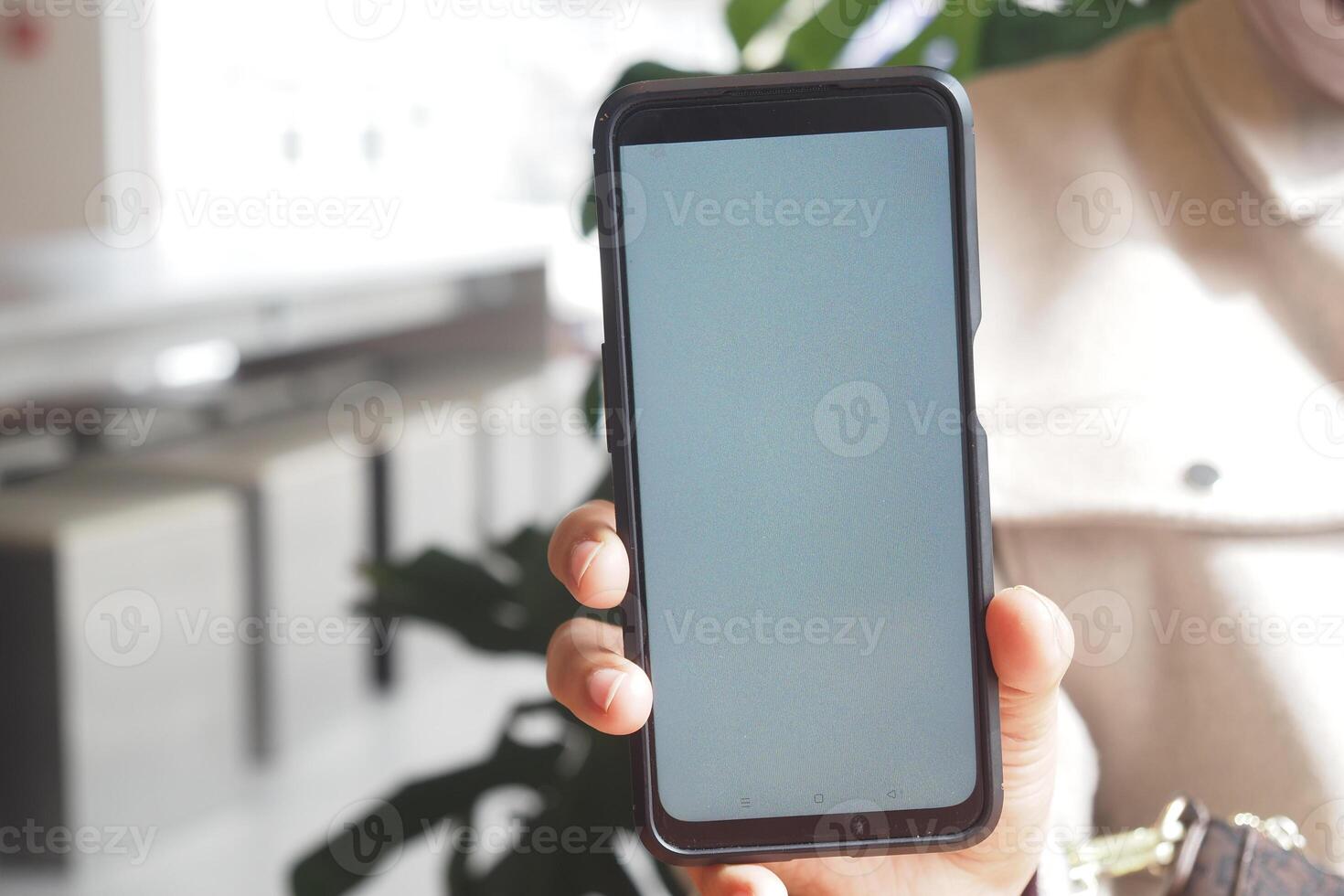 Holding a smartphone in a bright indoor setting near plants photo