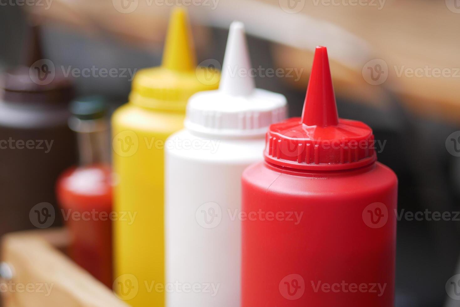 Colorful condiment bottles lined up on a rustic wooden table photo