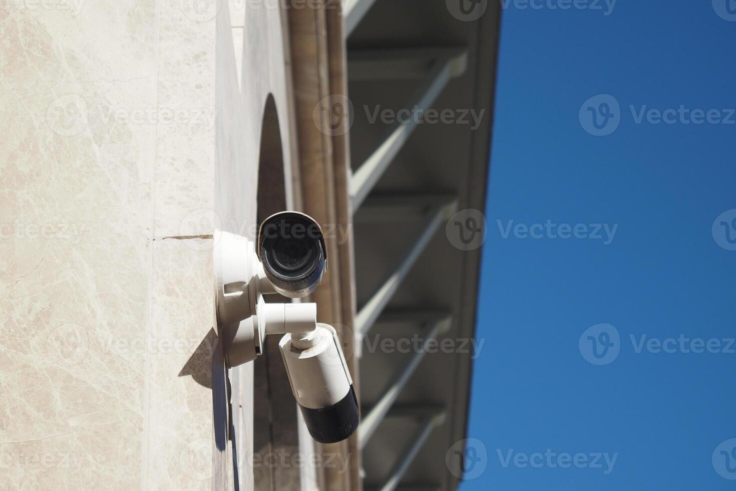 Security camera mounted on a building against a clear blue sky photo