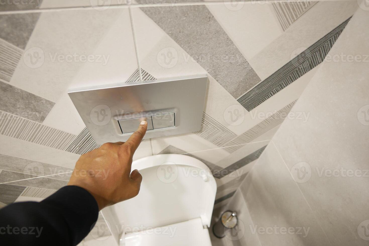 Hand pressing flush button in modern bathroom setting photo