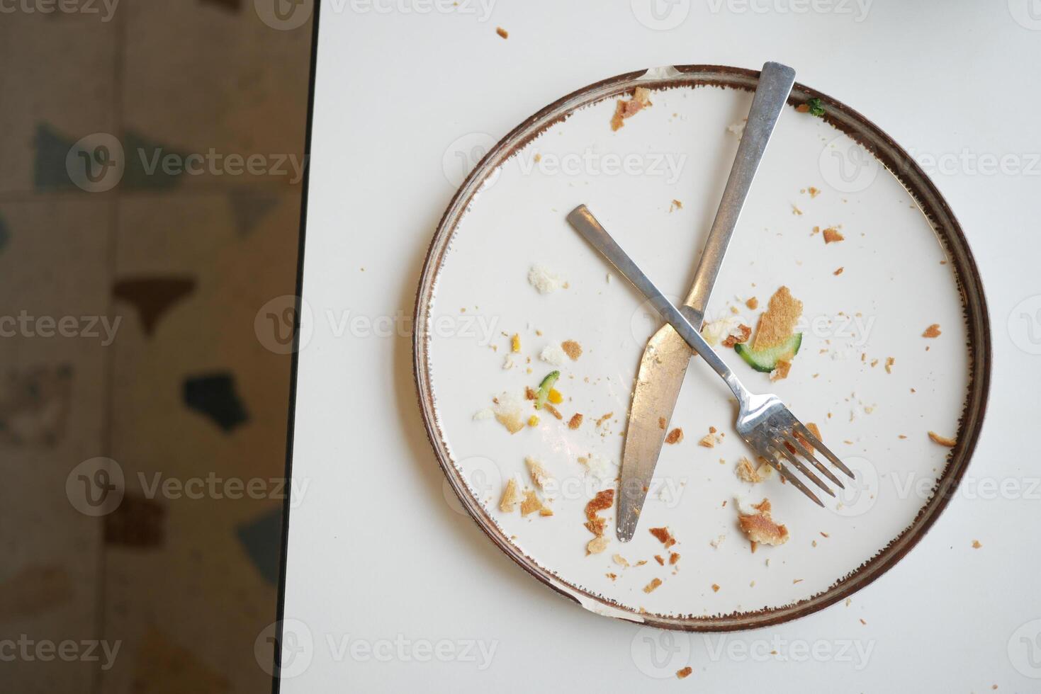 Leftover food remnants on a clean plate with utensils nearby photo