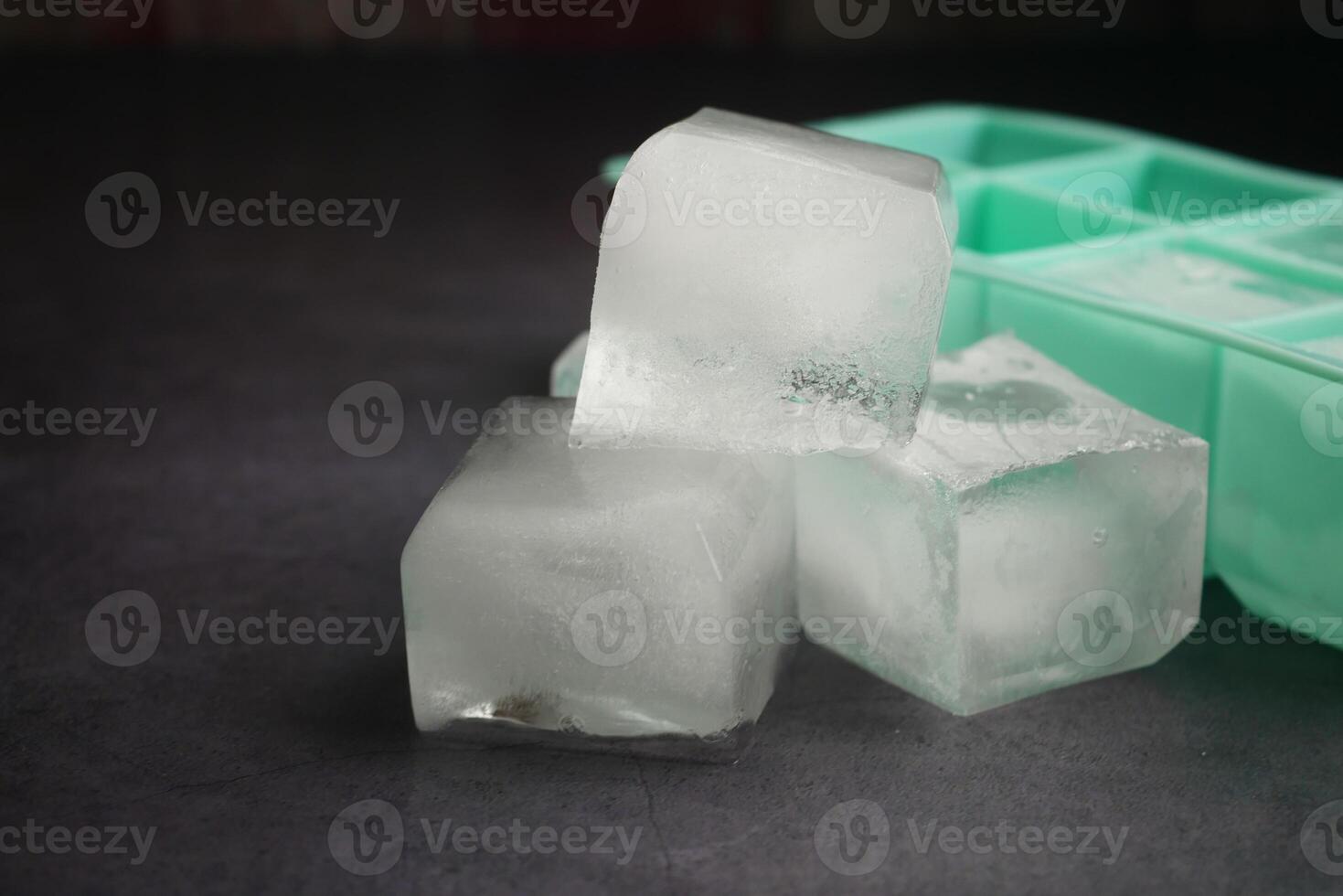 Ice cubes resting beside an ice tray on a dark surface photo