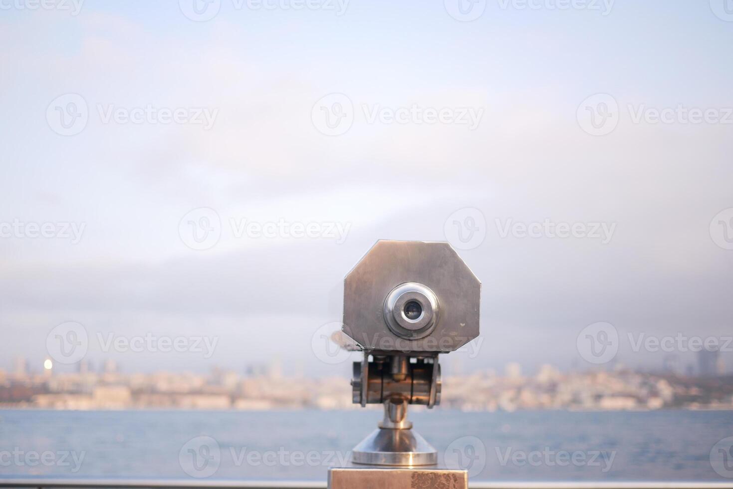 Metal telescope overlooks city skyline at dusk near waterfront photo