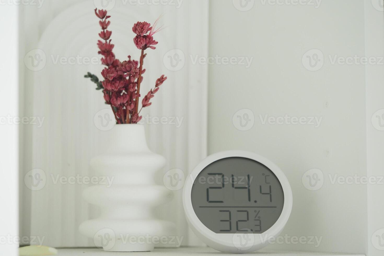 Decorative vase with dried flowers next to a temperature clock photo