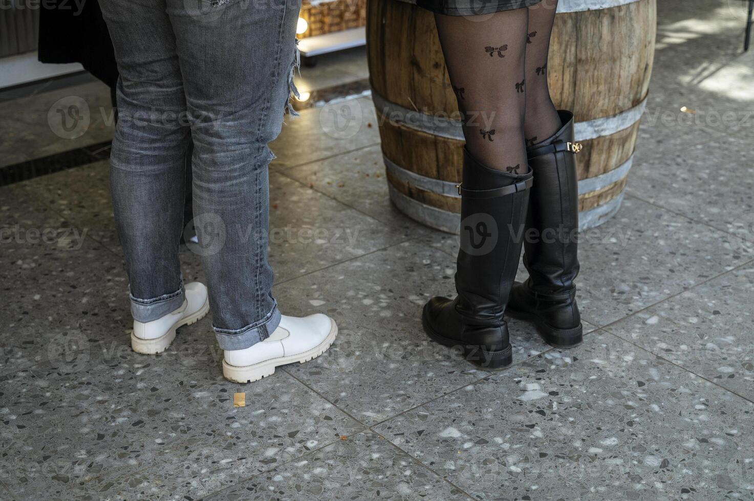 Two pairs of women's legs in autumn or spring close-up. One pair in tights and black high boots. The other in jeans and white shoes. photo