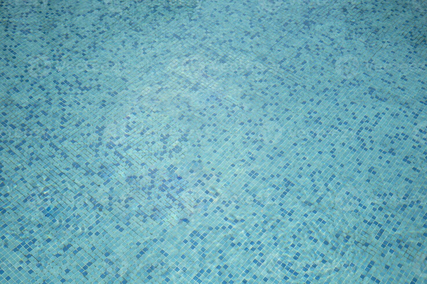 Crystal-clear water rippling over blue mosaic tiles in swimming pool. swimming pool pattern from top. pool water under the sunlight with blue mosaic, swimming pool surface. photo