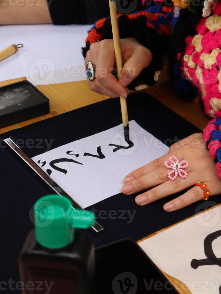 Person practicing calligraphy with brush and ink. Close-up of a person's hand delicately applying ink with a brush to a sheet of paper, practicing Chinese Calligraphy photo