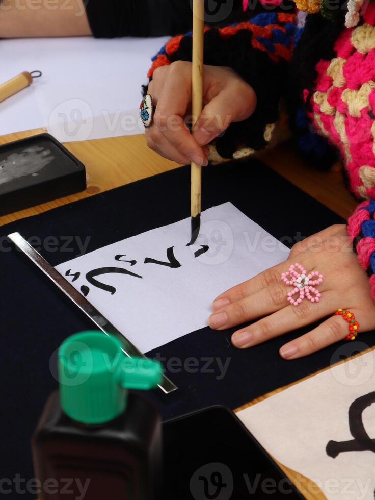 Person practicing Calligraphy with brush and ink. Close-up of a person's hand delicately applying ink with a brush to a sheet of paper, practicing Chinese calligraphy. photo