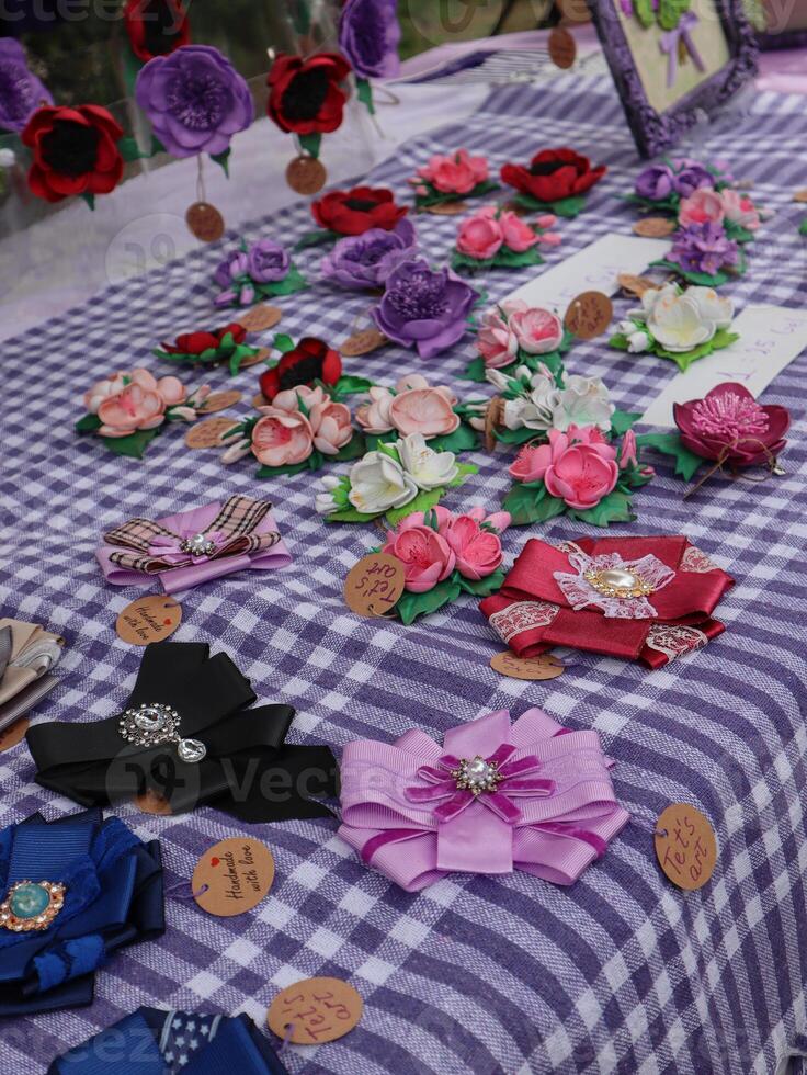 Handmade Floral Brooches and Bows at a Market Stall. A vibrant display of handmade flower brooches and bows, arranged on a checkered tablecloth at a market stall. photo