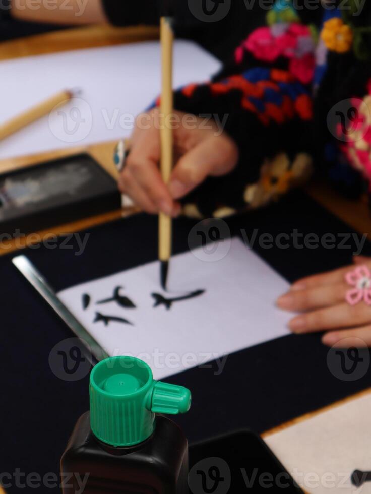 Person practicing calligraphy with brush and ink.Close-up of a person's hand delicately applying ink with a brush to a sheet of paper, practicing Chinese calligraphy. photo