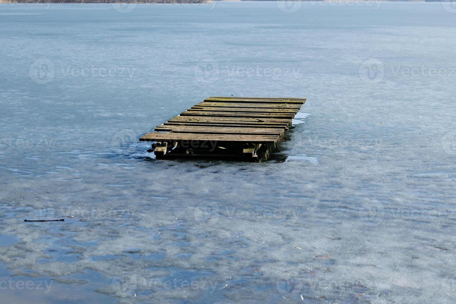 Old wooden pier on melting ice surface of frozen lake in early spring. Outdoor nature photography. Thaw season and changing weather. Design for banner, postcard, greeting card, wallpaper, poster photo