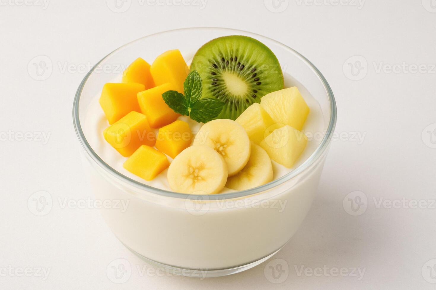 Bowl of creamy tropical greek yogurt topped with fresh mango, banana, pineapple, and kiwi slices, garnished with mint leaf photo