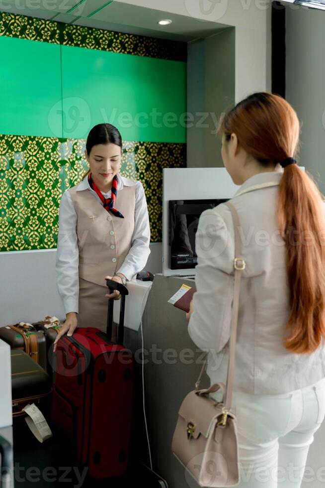 Female airline staff assisting passenger at check-in counter with luggage, passport and boarding pass before flight departure at modern airport terminal photo