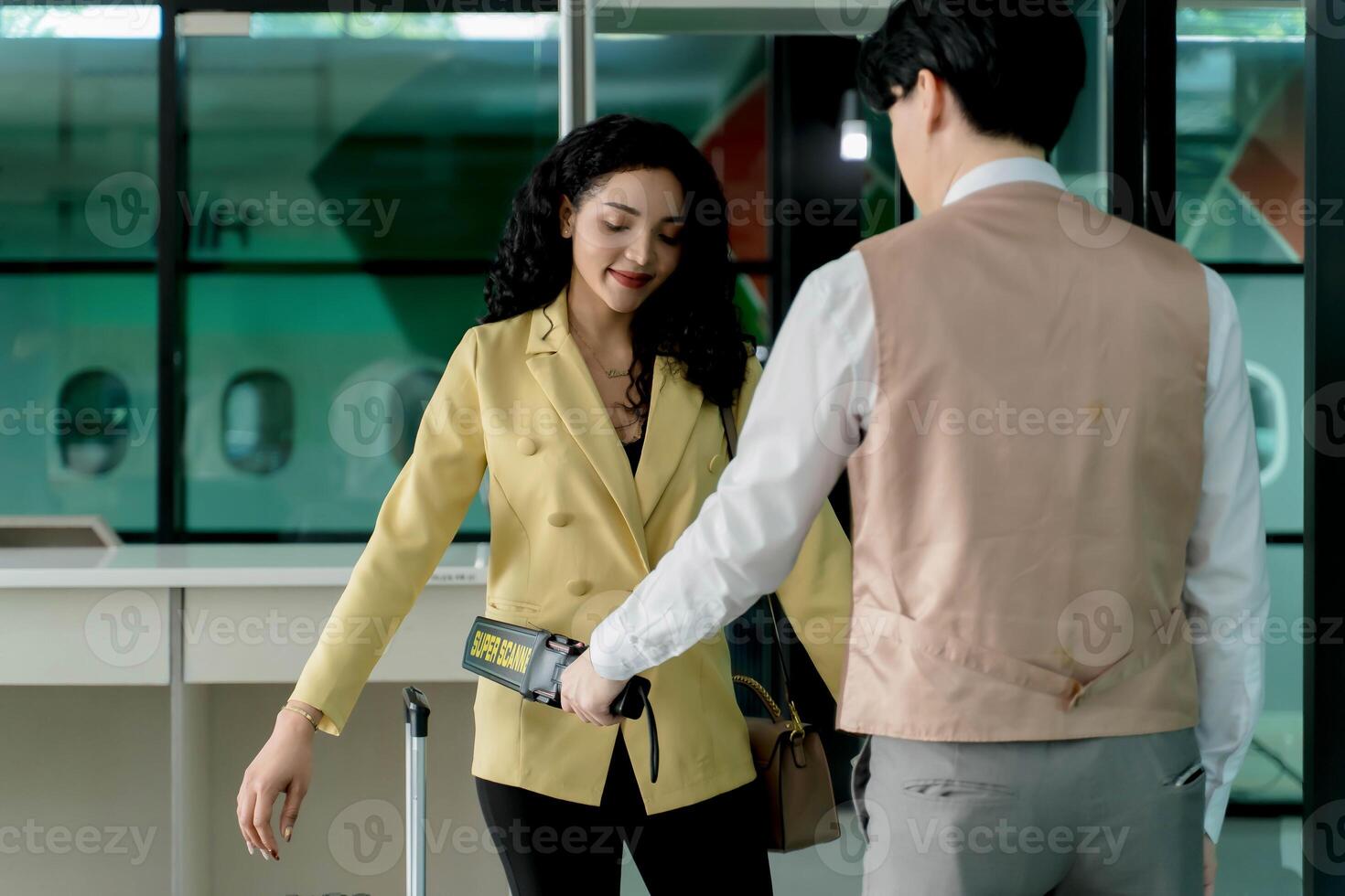 Airport security officer performing manual scan with handheld metal detector on female passenger during pre-boarding safety check at departure gate photo