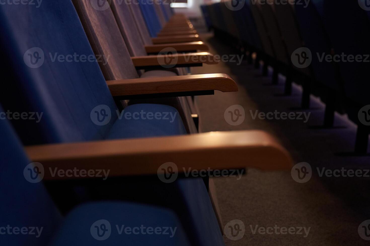 Some of the chairs are upholstered in fabric. A conference room with rows of empty blue chairs. With space to copy photo