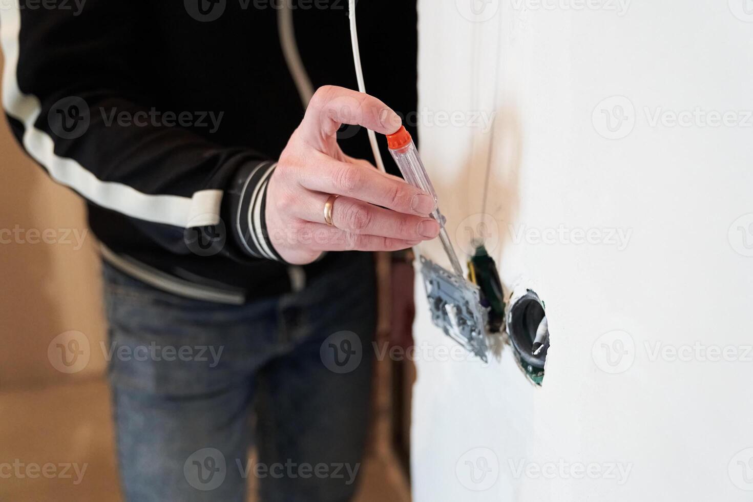 The man's hand checks the current in the junction box with electrical wires using an indicator screwdriver. The concept of repair and troubleshooting of an outlet. photo