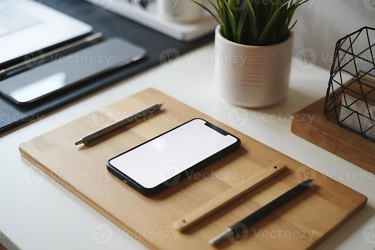 Minimalist workspace featuring mobile devices, pens, and greenery elements photo
