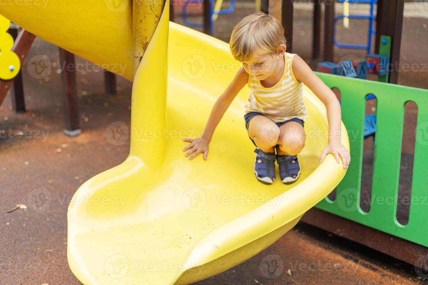 Boy crouching on yellow playground slide photo