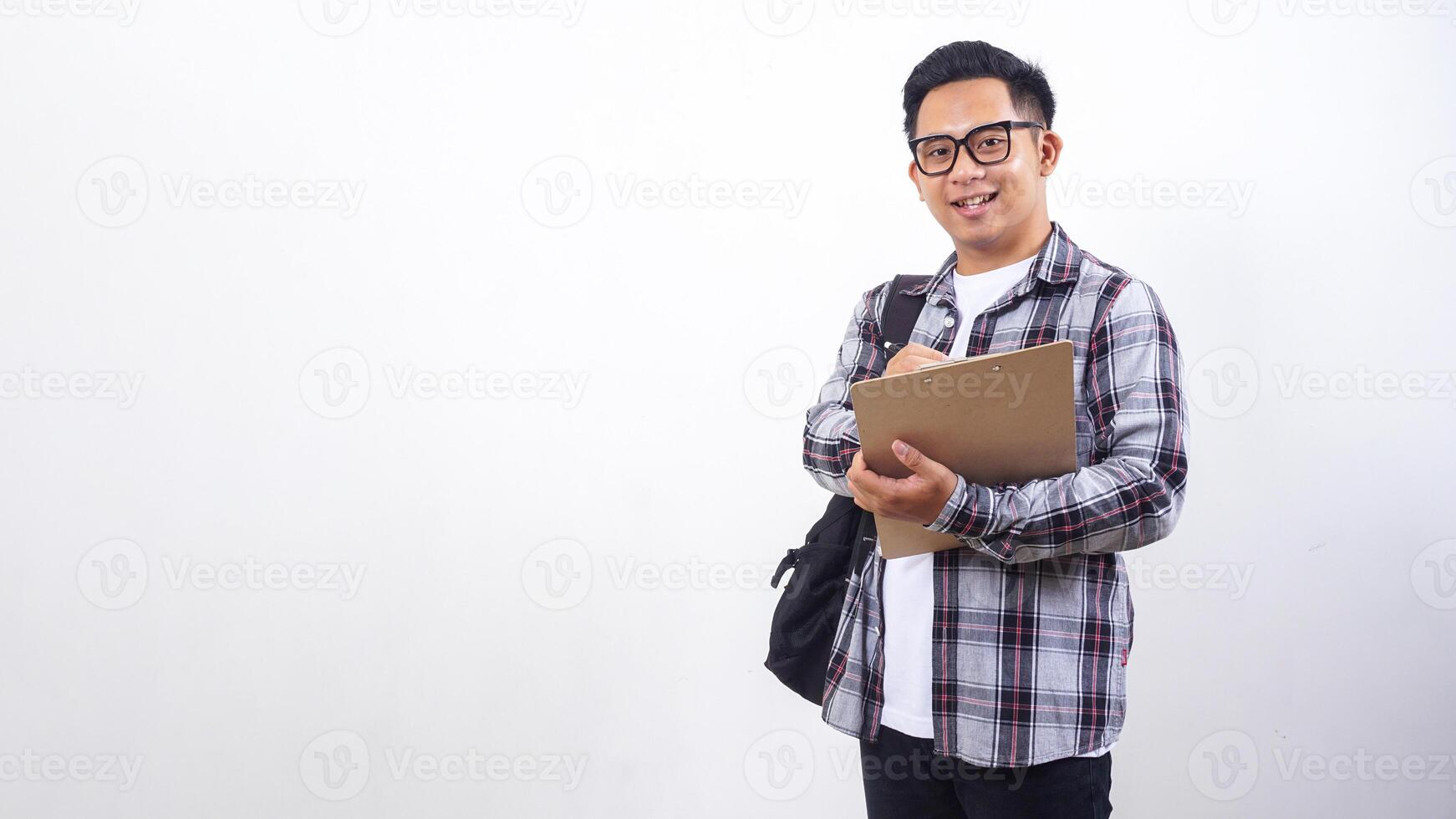 Smiling young Asian male college student with a backpack holding wooden clipboard and pen isolated on white background photo