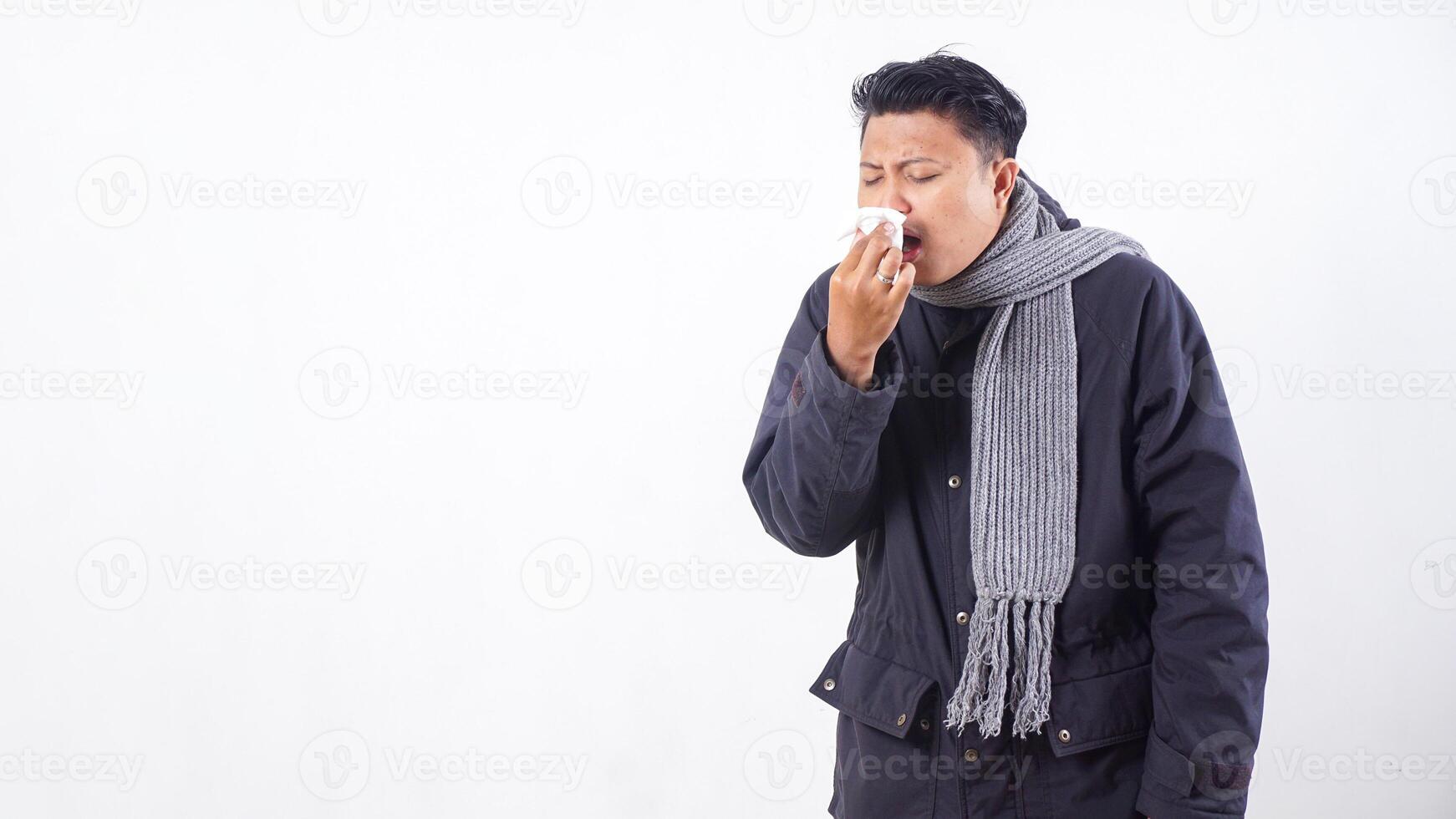 Unhealthy man wearing jacket blows his nose with tissue paper, suffering from flu isolated on white background photo