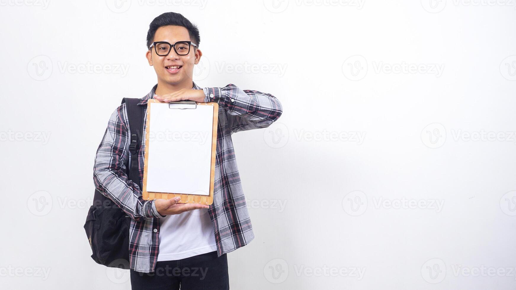 Portrait of smart young Asian male college student with a backpack holding clipboard with blank paper mock up isolated on white background photo