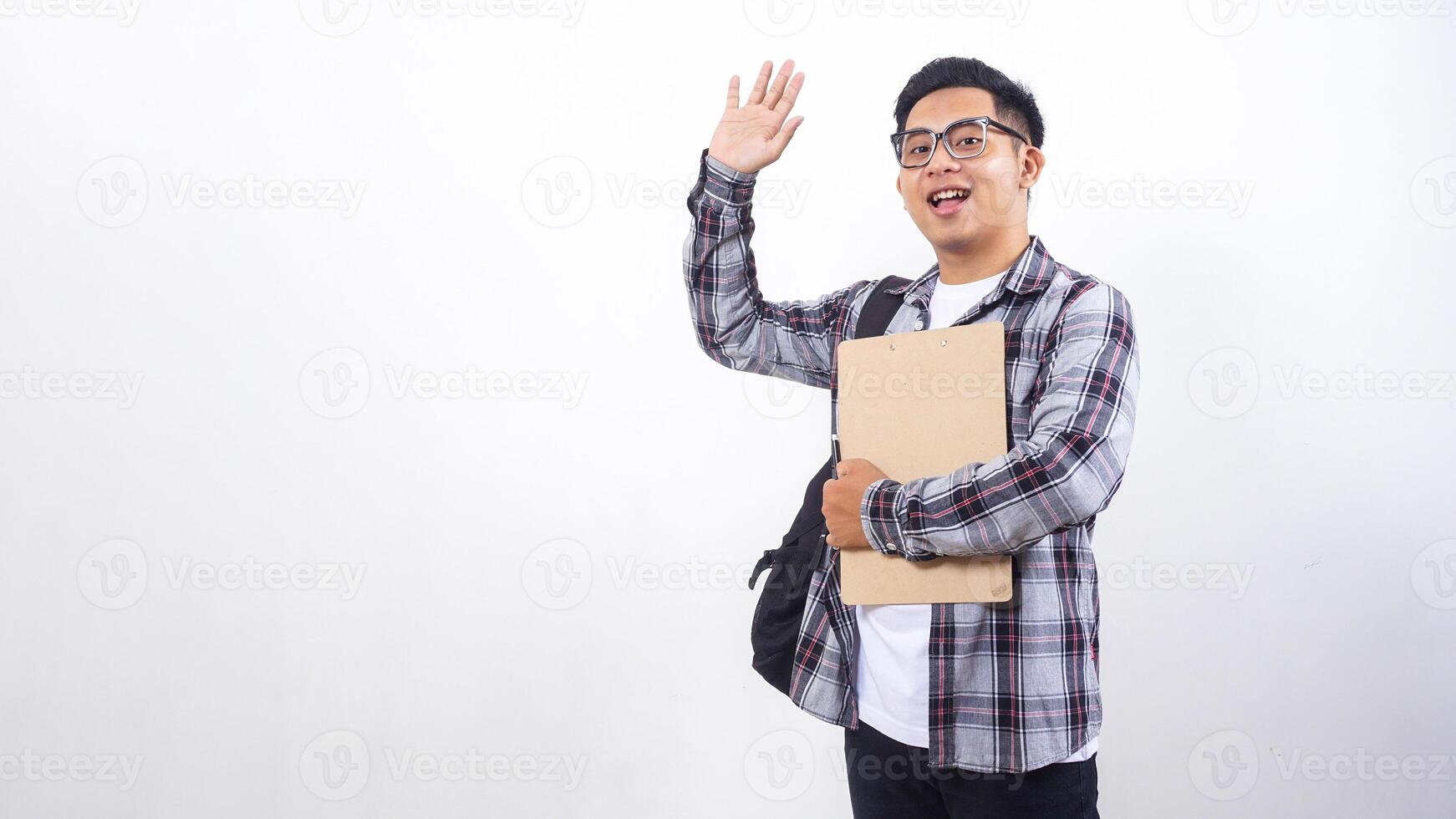 Young Asian male college student with a backpack holding wooden clipboard and pen while showing gesture of greeting isolated on white background photo