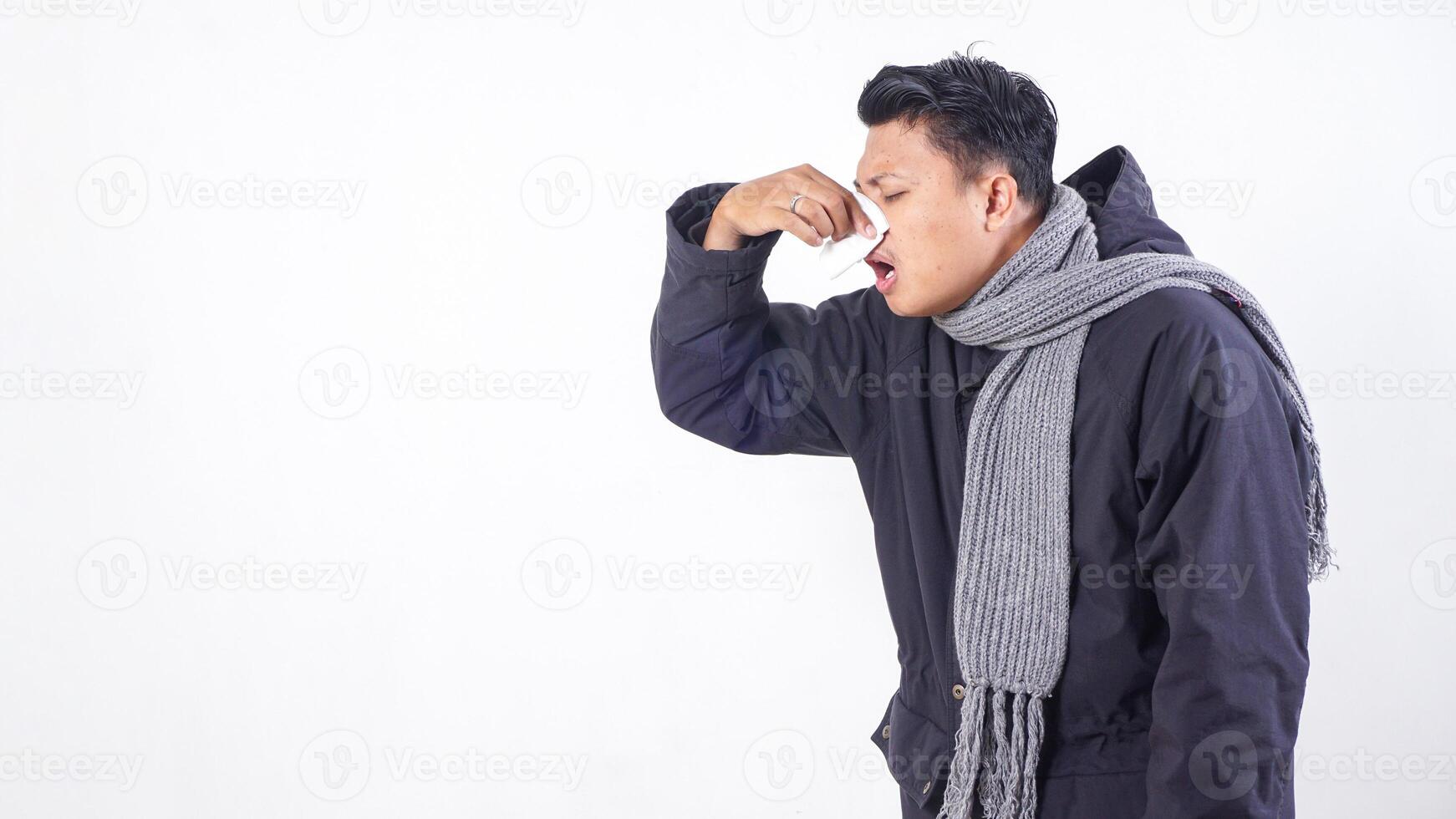 Sick man wearing jacket blows his nose with tissue paper, suffering from flu isolated on white background photo