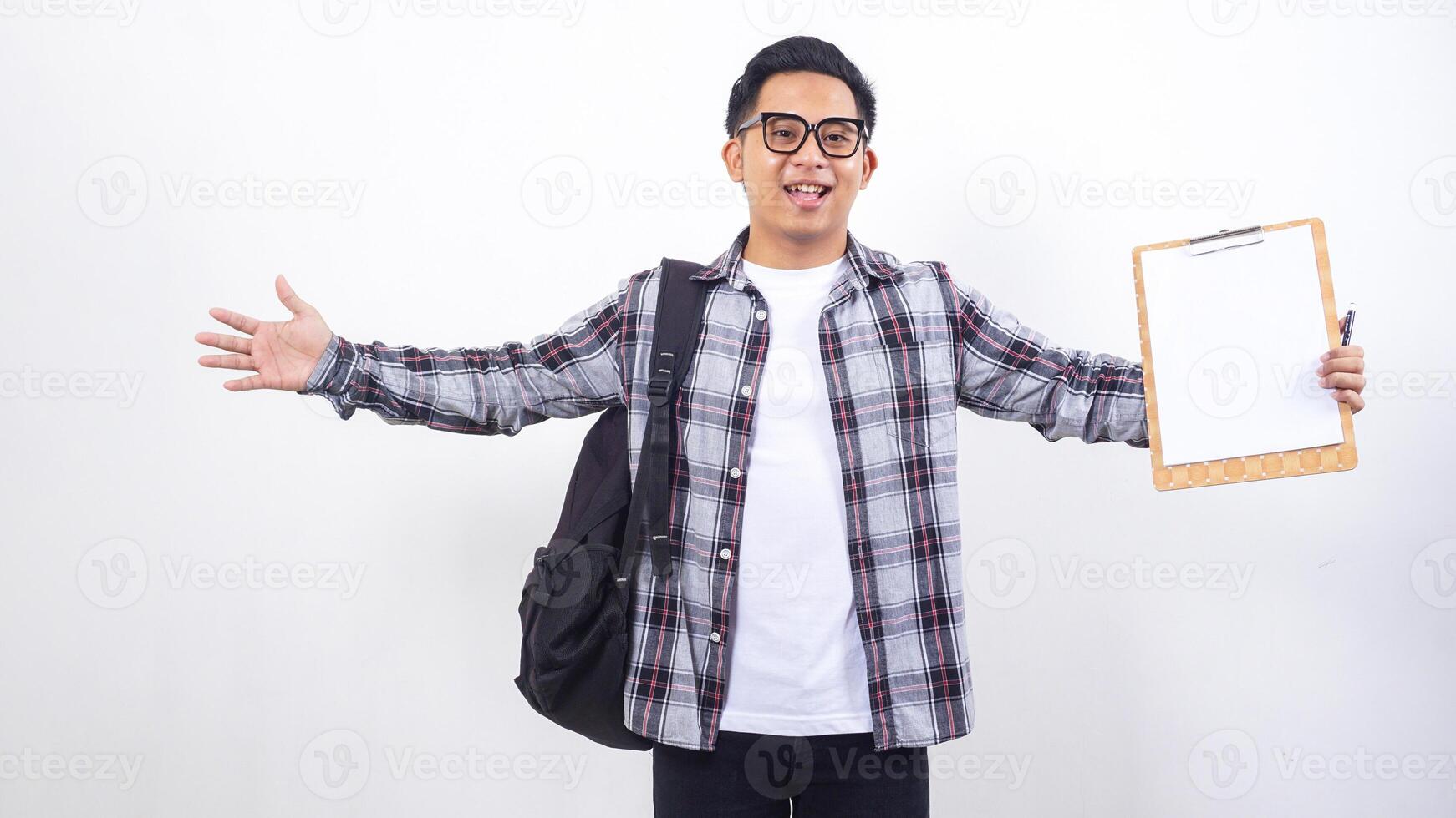 Young Asian male college student with a backpack holding clipboard with blank paper mock up isolated on white background photo