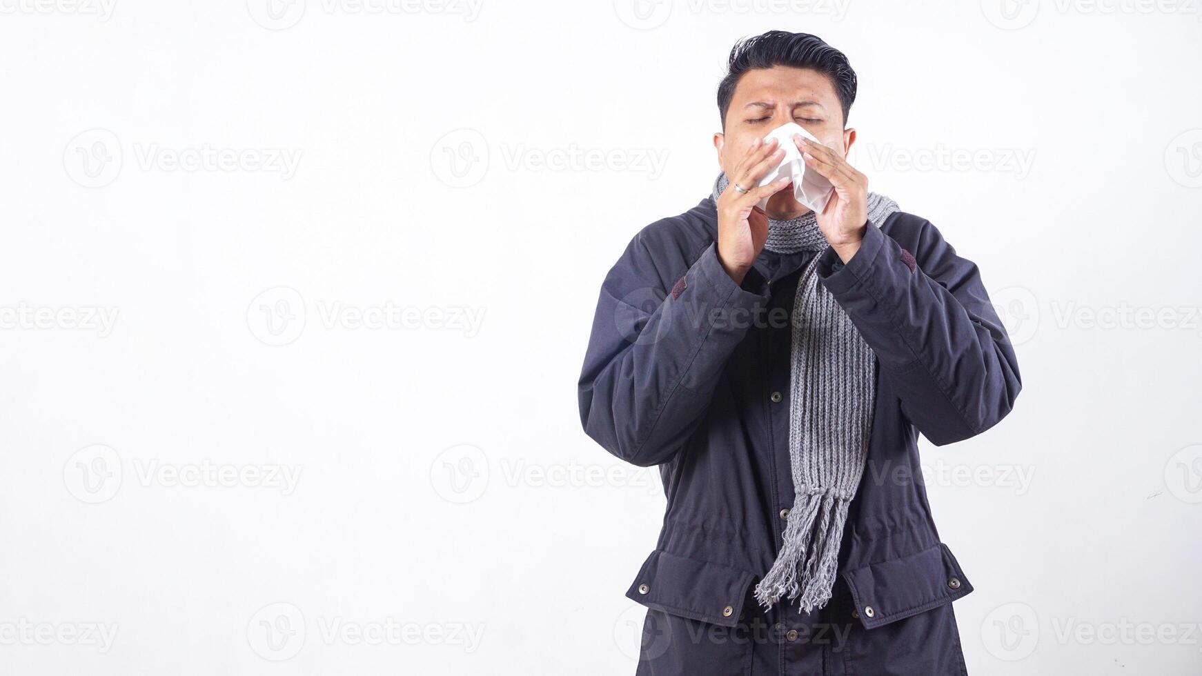 Unhealthy man wearing jacket is suffering from flu and sneezing using tissue paper isolated on white background photo