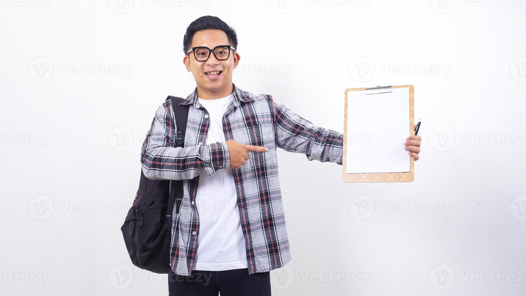 Happy young Asian male college student with a backpack holding clipboard with blank paper mock up isolated on white background photo
