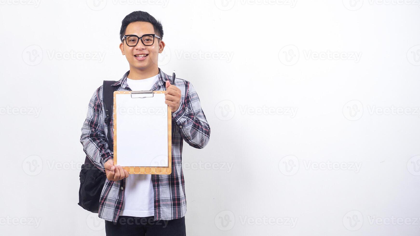 Portrait of handsome young Asian male college student with a backpack holding clipboard with blank paper mock up isolated on white background photo