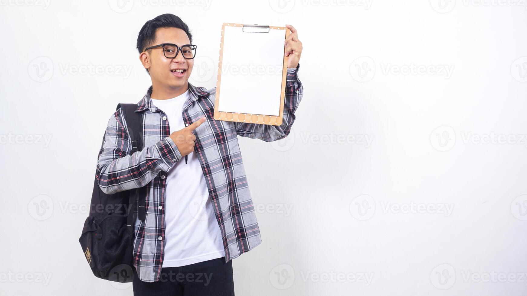 Portrait of smiling young Asian male college student with a backpack holding clipboard with blank paper mock up isolated on white background photo