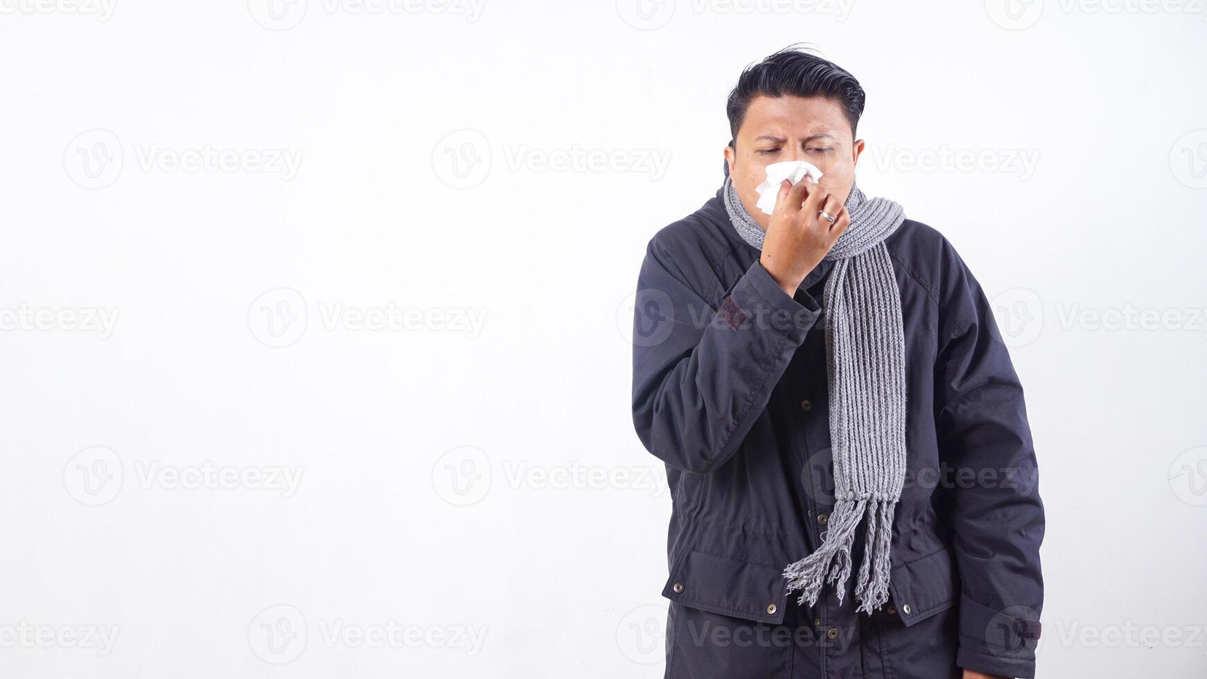 Portrait of sick man wearing jacket is suffering from flu and sneezing using tissue paper isolated on white background photo